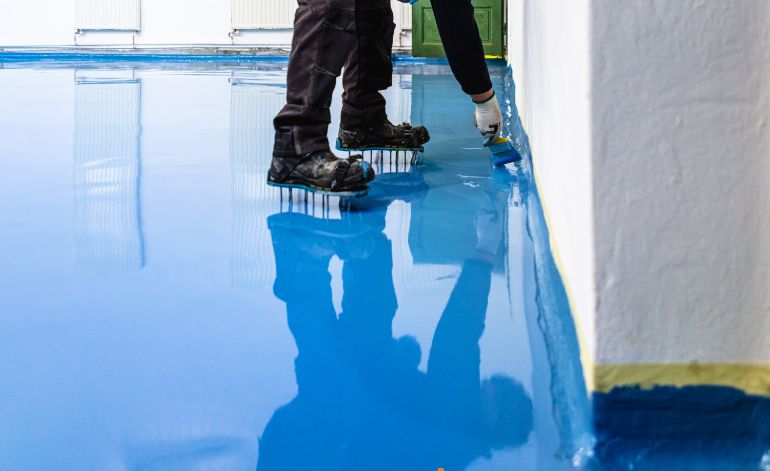 Individual painting a blue floor with a brush, representing epoxy flooring service in Springfield, Illinois.