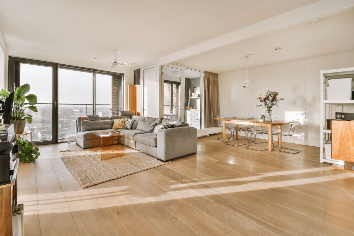A spacious living room featuring wooden floors and large windows, showcasing a bright and inviting atmosphere.